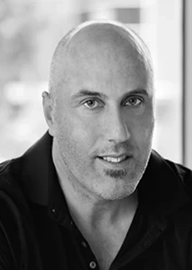 RE4ORM synthetic turf recycling – A man with a shaved head and trimmed goatee, wearing a dark collared shirt, looks directly at the camera with a slight smile. The background is softly blurred.