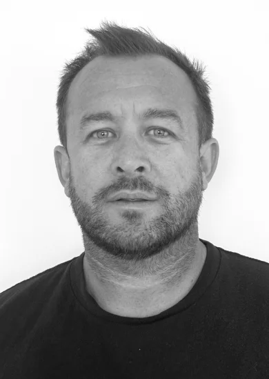 RE4ORM synthetic turf recycling – A man with short hair and a beard looks directly at the camera with a neutral expression, wearing a dark shirt against a plain white background.