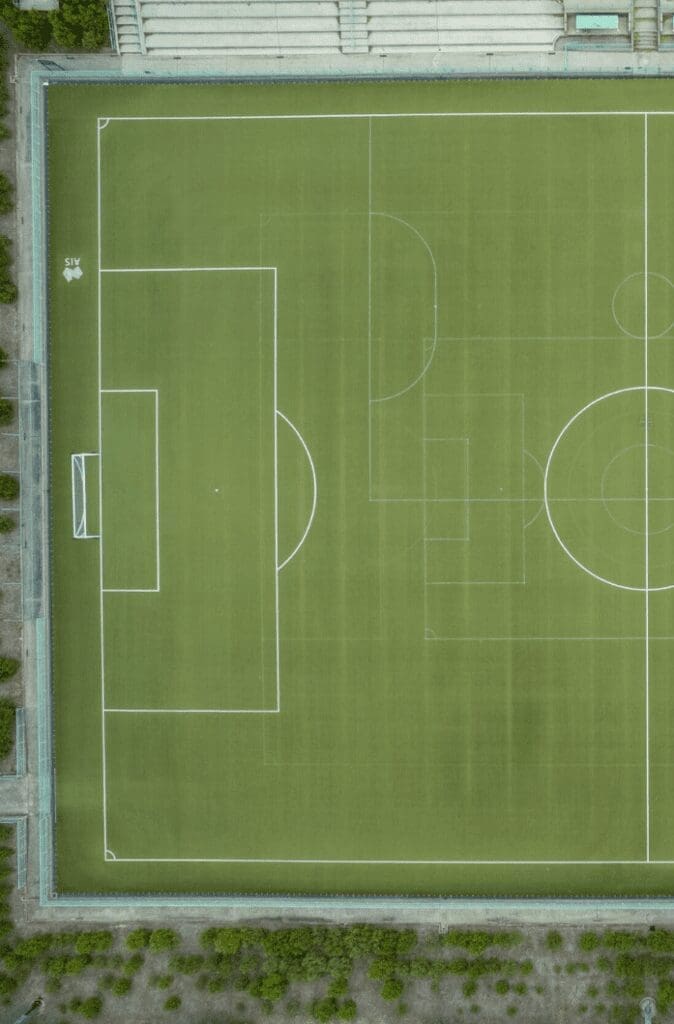 RE4ORM synthetic turf recycling &ndash; Aerial view of a green football pitch with white boundary lines, goalposts, and markings, surrounded by trees and pathways. The well-maintained pitch reflects the RE4ORM Process of continuous care and improvement.